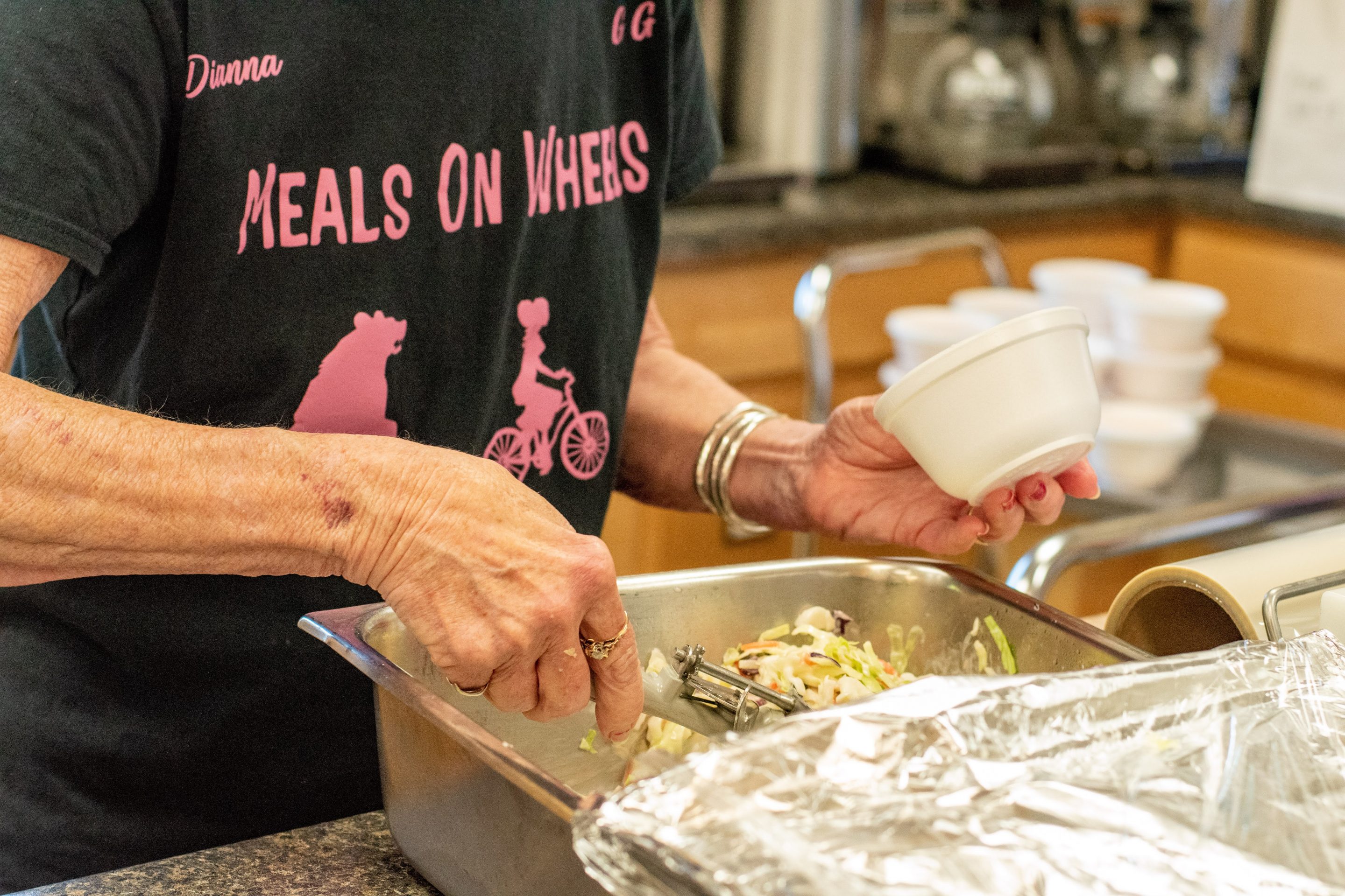 Volunteer scooping food into a to-go container for meal delivery